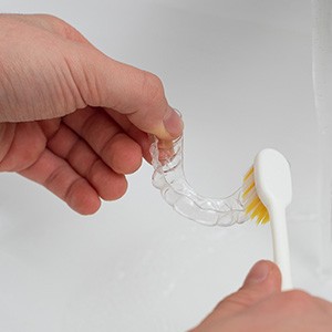 Patient cleaning clear aligner in sink