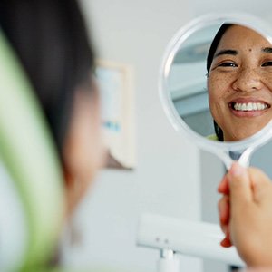 Woman smiling at reflection in handheld mirror